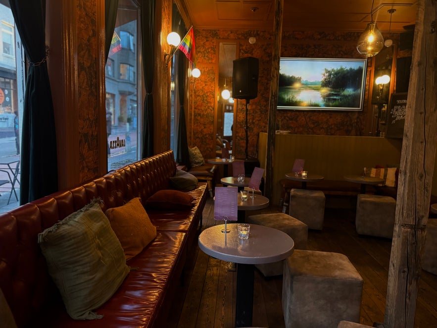 Cozy seating area inside Elly Bar featuring leather benches, soft pillows, vintage wallpaper, and dim amber lighting.