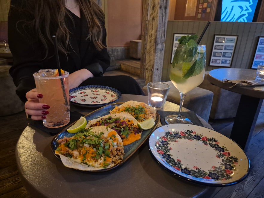 Table at Elly Bar in Reykjavik with a plate of tacos, cocktails, and decorative plates in a cozy bar setting.