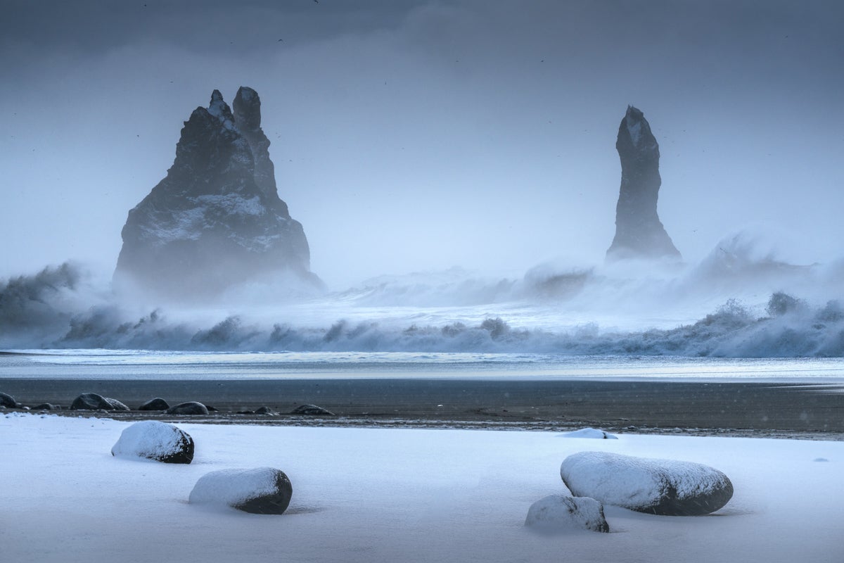 Snow covers a black sand beach on the South Coast of Iceland with sea stacks visible in the distance.