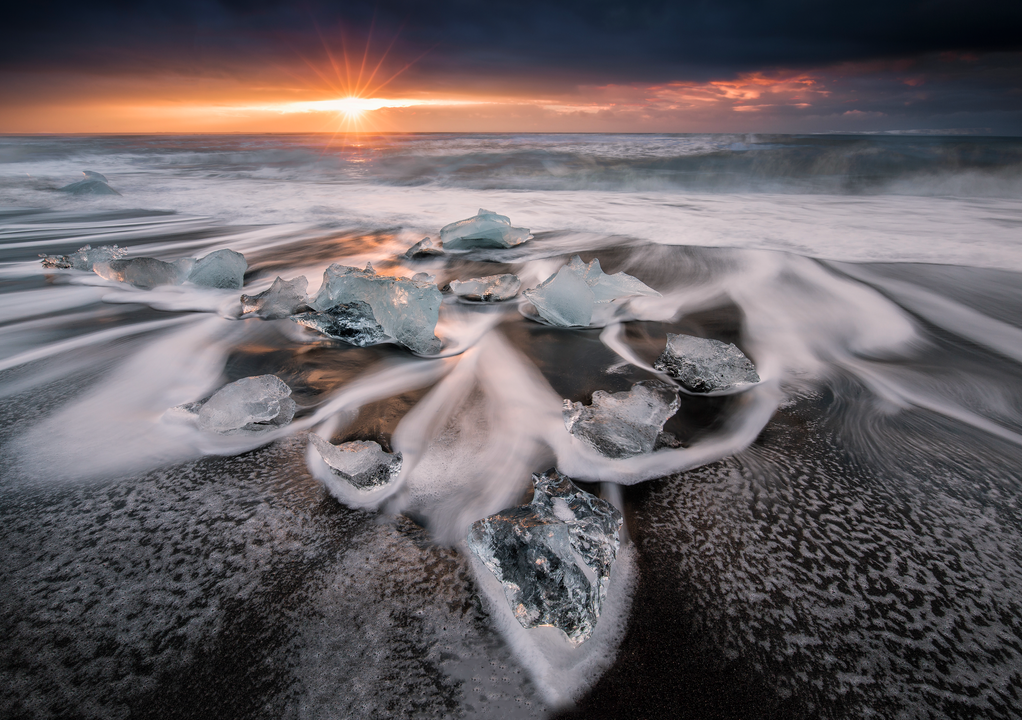 Ice chunks scattered along Diamond Beach as ocean waves flow around them at sunrise.