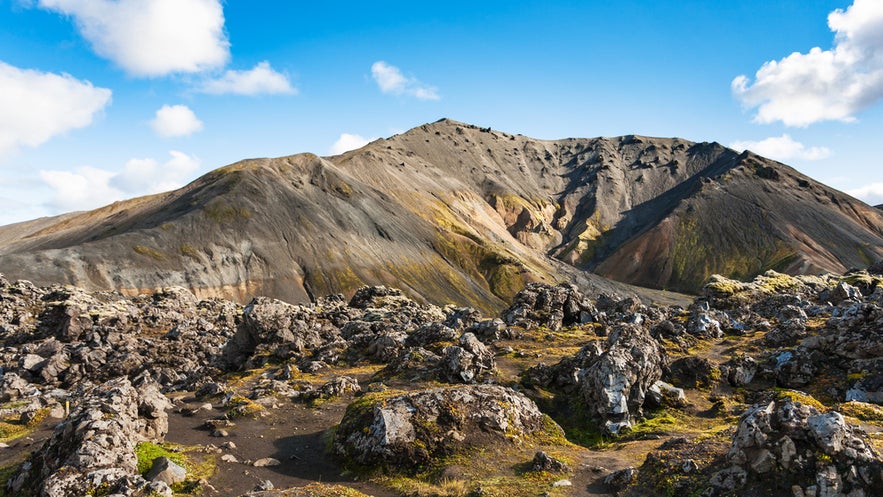 View of Laugahraun Lava Field with dark volcanic rocks and Blahnukur Mountain in Landmannalaugar, Iceland.