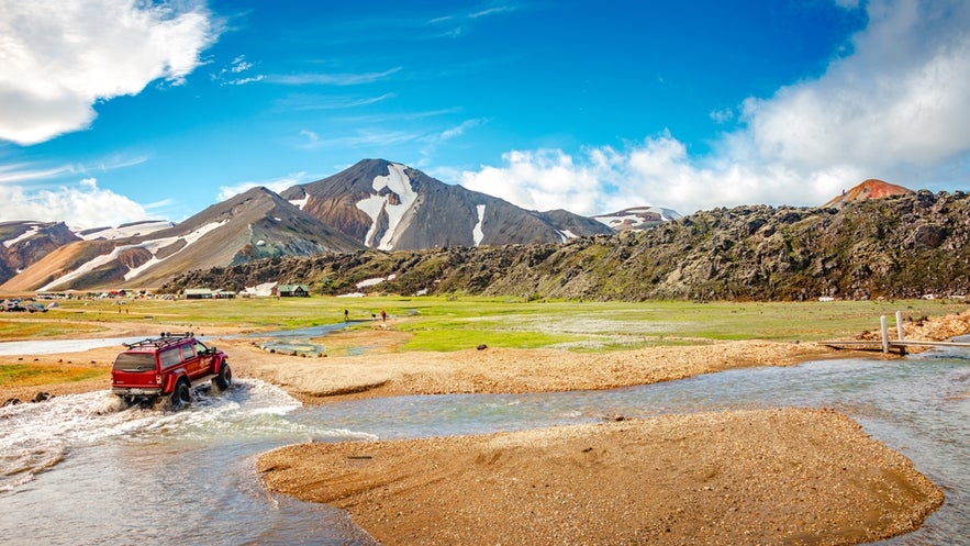 4x4 vehicle crossing a river near Landmannalaugar Campsite in Iceland’s Highlands, with Blahnukur Mountain in the background.
