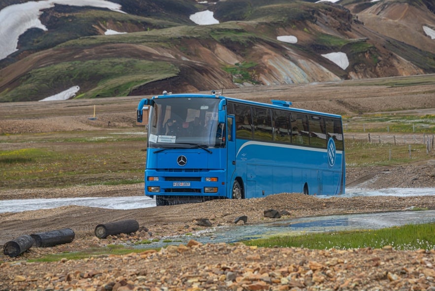 Highland bus driving through a river near Landmannalaugar, Iceland, offering guided transport across remote F-roads.