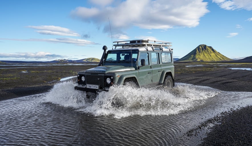 4x4 vehicle crossing a river on F208 road to Landmannalaugar, Iceland, surrounded by volcanic mountains and black sand plains.