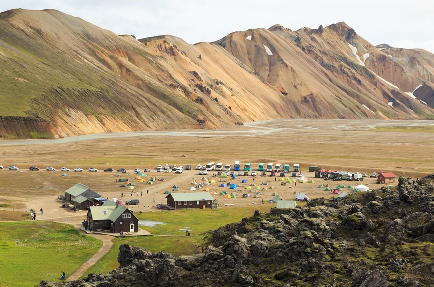 Aerial view of Landmannalaugar Campsite in Iceland’s Highlands with tents, cars, and colorful rhyolite mountains.