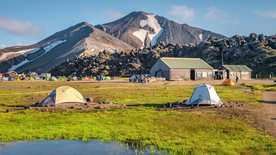 Landmannalaugar Campsite with tents and mountain huts in Iceland’s Highlands, set against Blahnukur’s snow-capped peak.