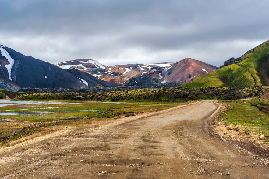 Gravel road leading to Landmannalaugar, Iceland, surrounded by colorful rhyolite mountains and moss-covered lava fields.