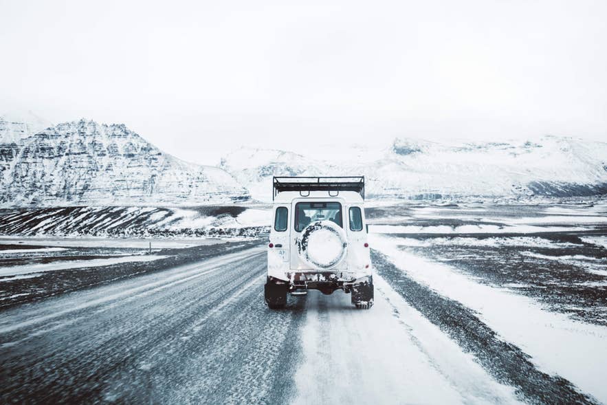 White 4x4 driving on a snow-covered road through Icelandic mountains
