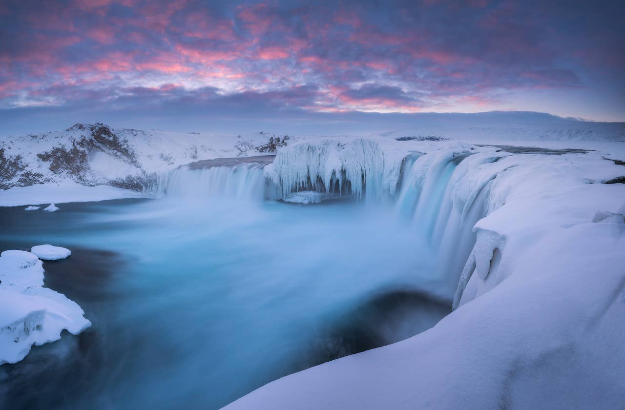 Godafoss waterfall flows through a rocky canyon in North Iceland under soft daylight.