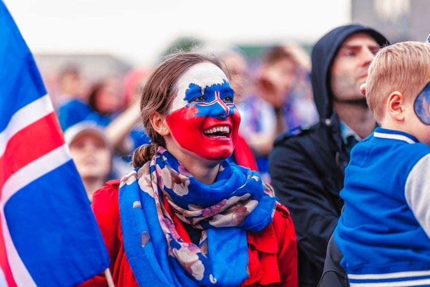 Icelander woman with Iceland flag face paint smiling in Reykjavik during national celebration.