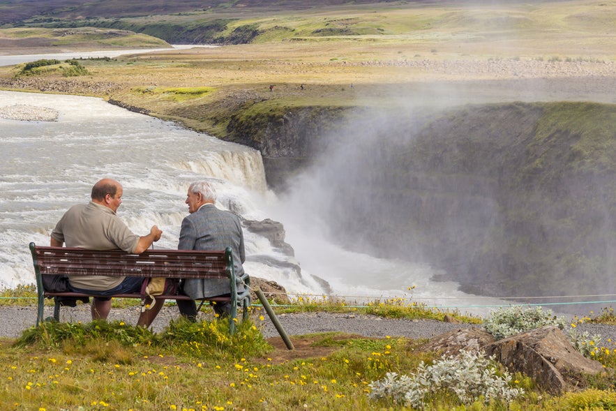 Icelanders sitting on a bench enjoying the view of Gullfoss Waterfall in Iceland’s Golden Circle.