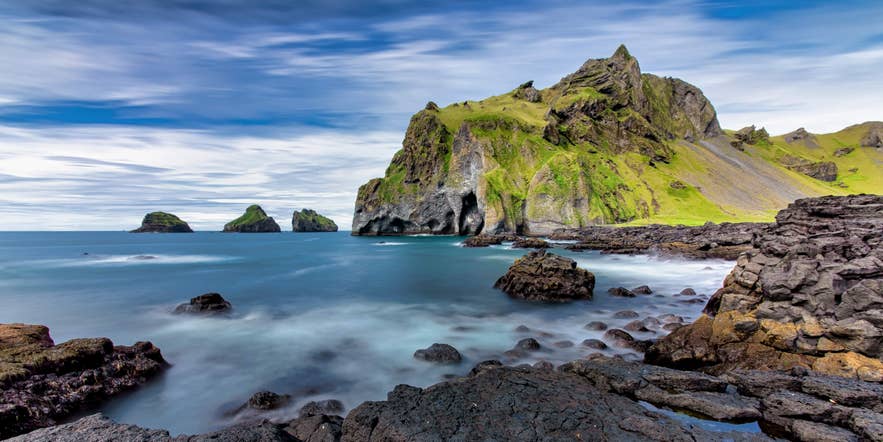 Westman Islands in Iceland with rugged green cliffs and volcanic rocks by the sea.