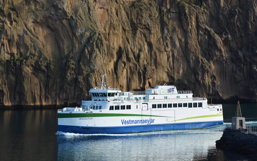 เรือเฟอร์รีเฮอร์ยอลฟูร์กำลังเดินทางถึงเกาะเฮมาเอย์ในหมู่เกาะเวสต์แมน ประเทศไอซ์แลนด์ โดยมีหน้าผาภูเขาไฟอยู่ด้านหลัง