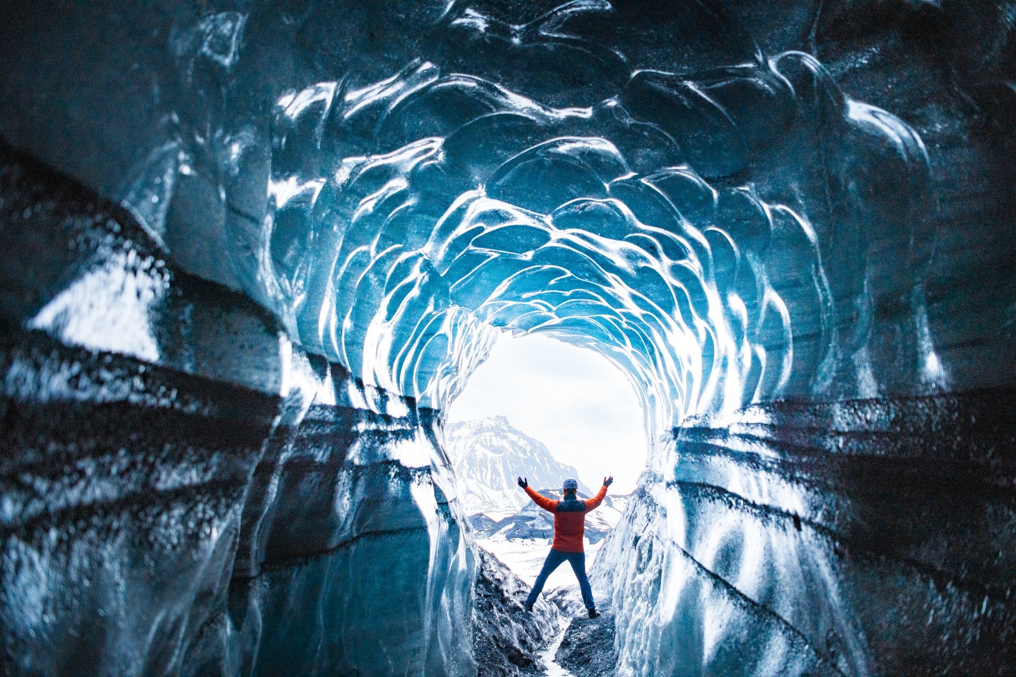 Eventyrer, der løfter armene inde i en frossen blå tunnel i Katla-isgrotten.