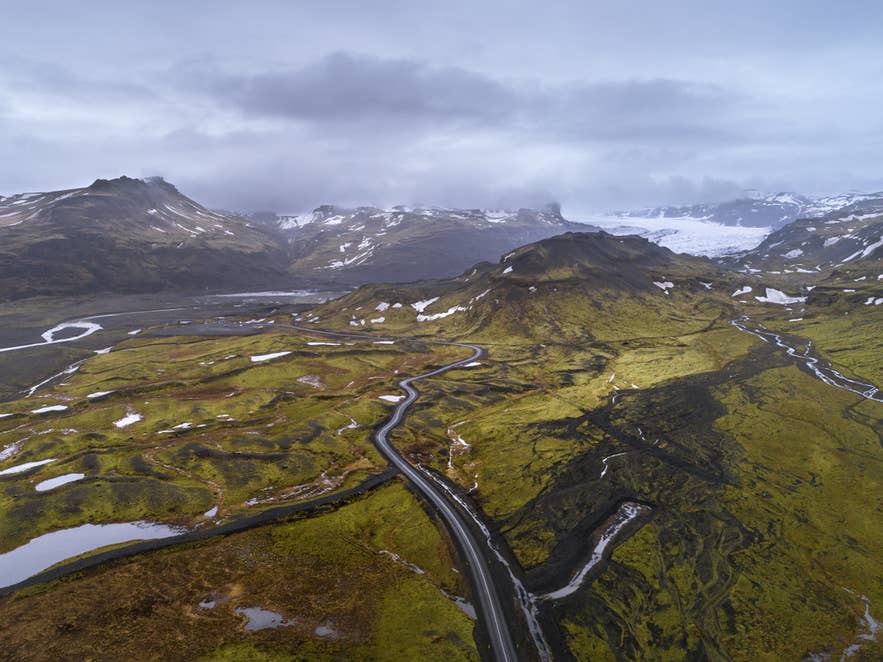 Ilmakuva Sólheimajökull-jäätikölle johtavasta tiestä Etelä-Islannissa, joka kiemurtelee sammaleisen vulkaanisen maaston halki kohti jäisiä huippuja.