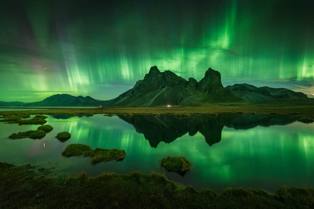 Polarlichter tanzen über einer Bergkette mit Blick auf einen See in Ostisland.