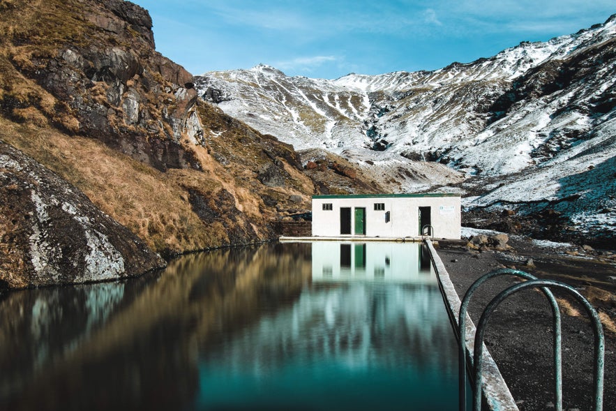 Seljavallalaug swimming pool in a mountain valley on Iceland’s South Coast with snow-covered peaks in the background.