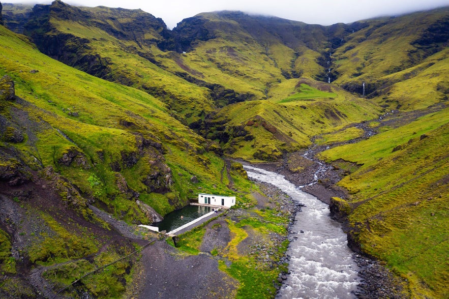 Det geotermiske bassin Seljavallalaug i Island omgivet af gr&oslash;nne bjerge og en rindende flod.
