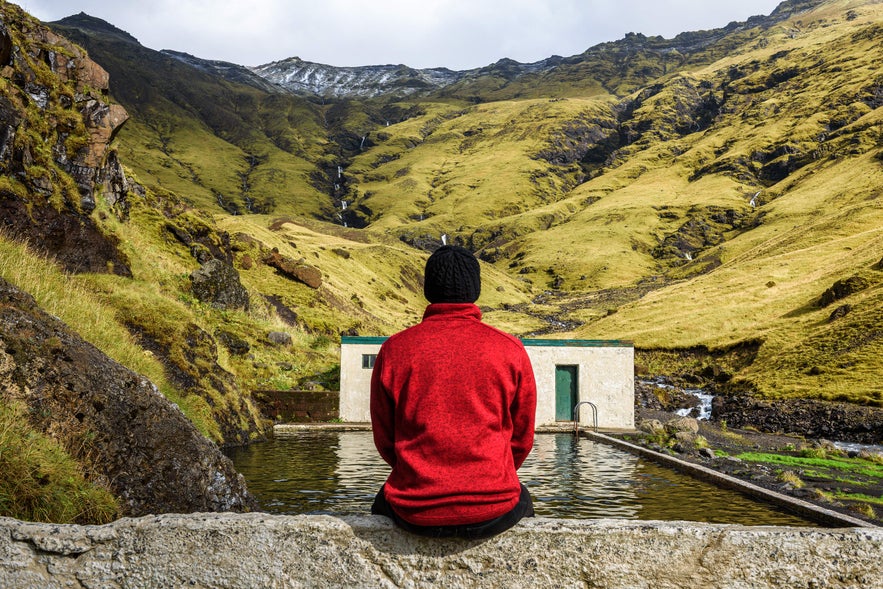 Person sitting by Seljavallalaug geothermal pool in Iceland.