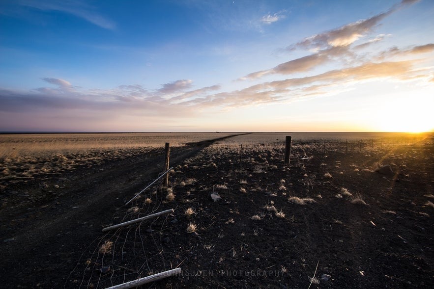 Sunrise over an open gravel road on Sólheimasandur plain in South Iceland with golden light and blue sky