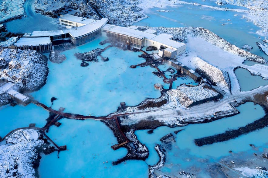 Vista aerea di un complesso termale geotermico in inverno, lagune blu circondate dalla neve e edifici moderni in Islanda.