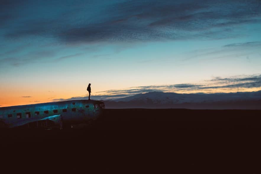 Voyageur debout sur l'épave du DC3 à Solheimasandur Beach au coucher du soleil dans le sud de l'Islande.