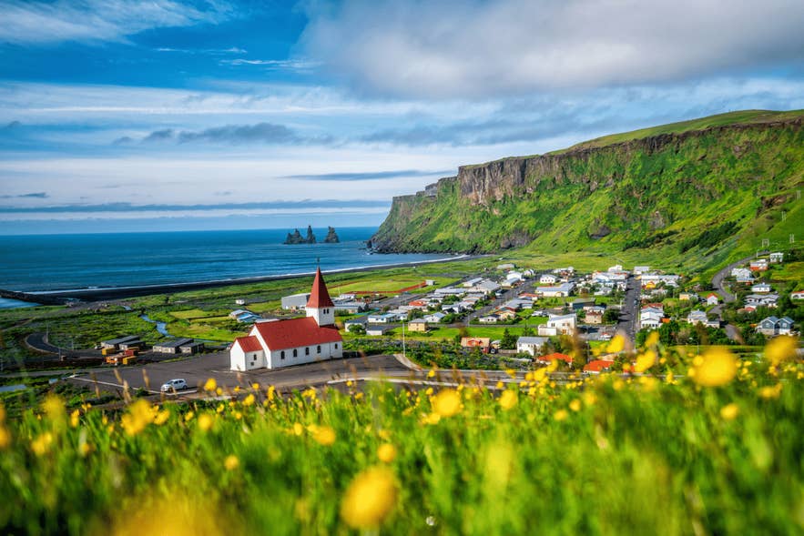 Vue estivale de Vik, village du sud de l'Islande avec son église sur la colline et les aiguilles de Reynisdrangar sur la côte.