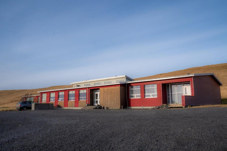 Volcano Hotel, a red building set against a hill, located near the Solheimasandur DC3 Plane Wreck.