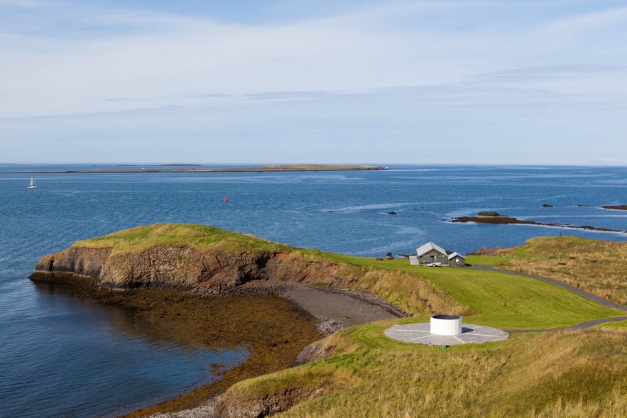 Coastal view of Videy Island with grassy cliffs and the Imagine Peace Tower, overlooking calm blue waters. Coastal view of Videy Island with grassy cliffs and the Imagine Peace Tower, overlooking calm blue waters.