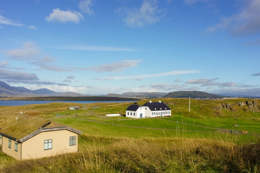 Scenic view of Videy Island with grassy fields, white buildings, and distant mountains under a partly cloudy blue sky. Scenic view of Videy Island with grassy fields, white buildings, and distant mountains under a partly cloudy blue sky.