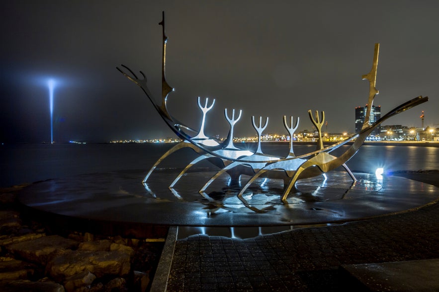 Sun Voyager sculpture in Reykjavik glows at night, with city lights and Imagine Peace Tower’s beam across the water. Sun Voyager sculpture in Reykjavik glows at night, with city lights and Imagine Peace Tower’s beam across the water.