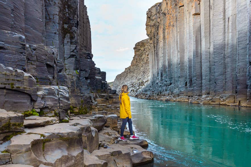 Eine Reisende im gelben Mantel bewundert den Studlagil-Canyon, eines der Naturwunder Islands