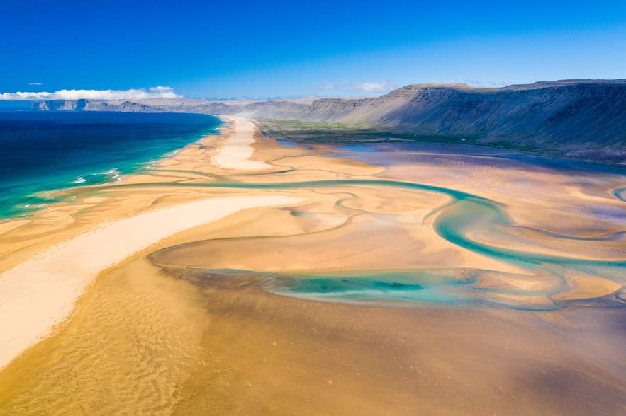 Der Raudasandur-Strand leuchtet mit gold-rotem Sand und türkisfarbenem Wasser – ein idyllisches Beispiel für Islands Naturschönheit
