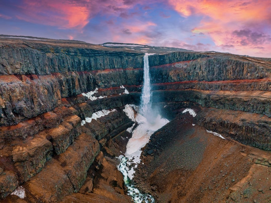 Hengifoss Waterfall drops over red-striped cliffs in East Iceland, a striking display of the natural wonders of Iceland