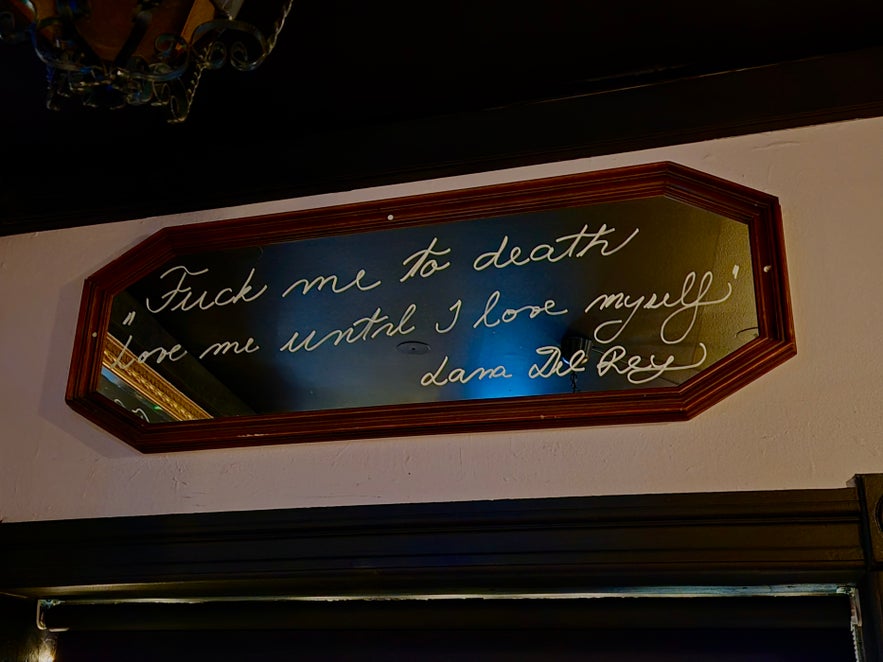 Framed mirror at 22 Bar featuring handwritten cursive text and warm interior lighting reflected on its surface. Framed mirror at 22 Bar featuring handwritten cursive text and warm interior lighting reflected on its surface.
