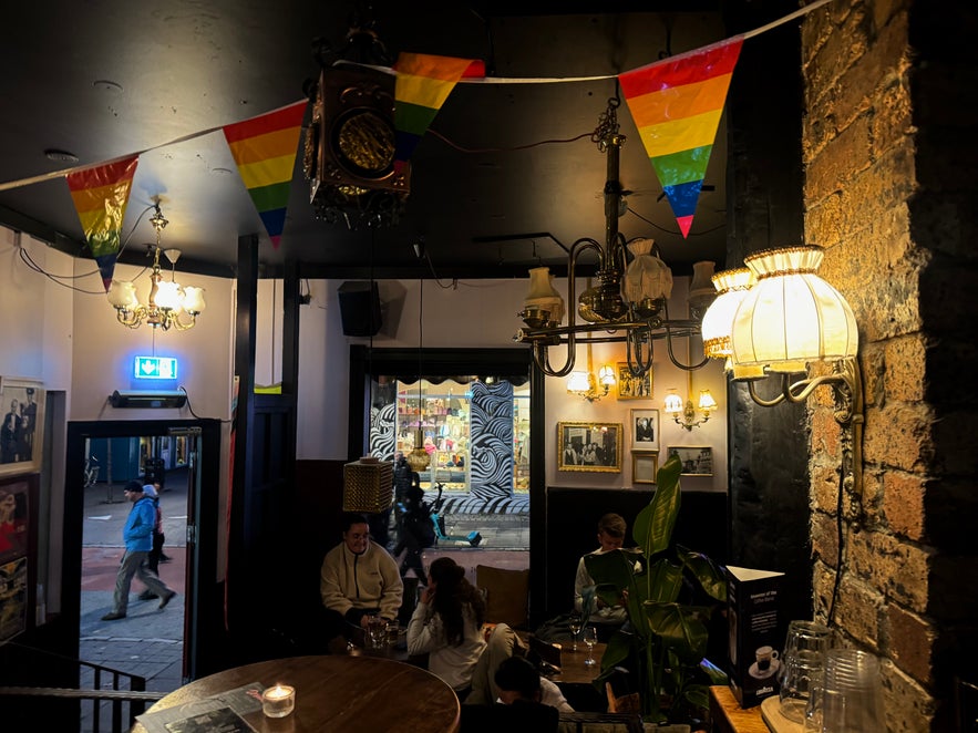 Inside 22 Bar in Reykjavik, with rainbow pride bunting, vintage lamps, and groups of people chatting at candlelit tables.