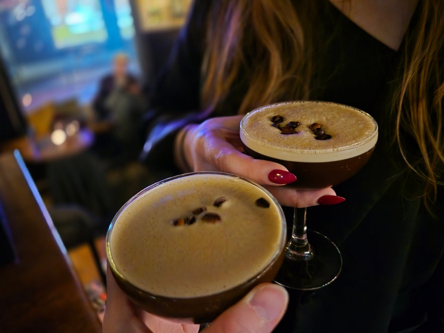 Two espresso martinis garnished with coffee beans, held up for a toast inside 22 Bar.