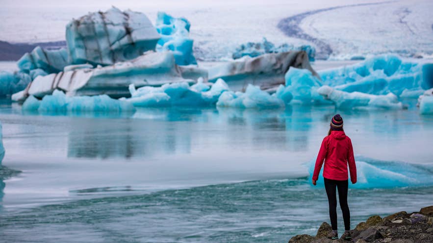 Eine Reisende betrachtet die treibenden Eisberge in der Gletscherlagune Jökulsarlon, die zu den atemberaubendsten Naturwundern Islands zählt.