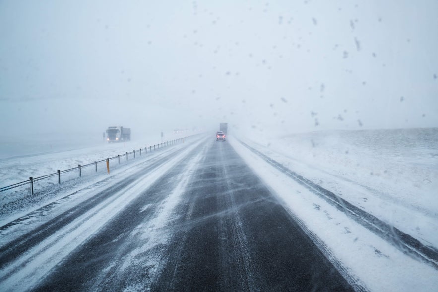 Vehicles traveling down a snowy road in Iceland, emphasizing the need for caution during winter weather conditions.