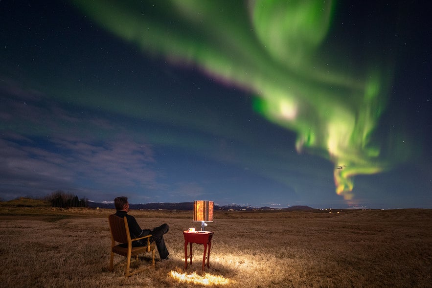 A man sitting in a chair watching the northern lights in Iceland, enjoying the view safely during clear weather.