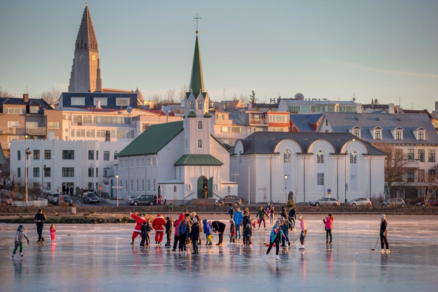 People ice skate on frozen Tjornin Pond in Reykjavik, with Frikirkjan Church and Hallgrimskirkja Church in the background.