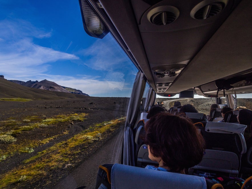 Tourists on a bus driving through Iceland’s volcanic landscape, enjoying scenic views during a stopover in Iceland.