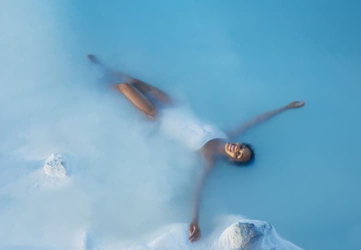 Woman relaxing in the warm blue waters of the Blue Lagoon, a must-visit destination during a layover or stopover in Iceland.