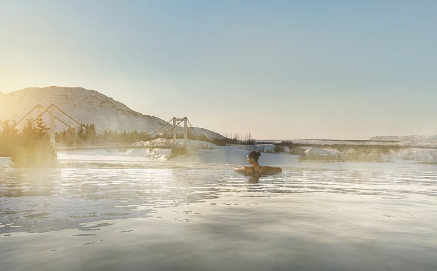 Eine Besucherin genießt das warme Wasser der Laugaras Lagoon, umgeben von malerischen Bergen und üppiger Landschaft.