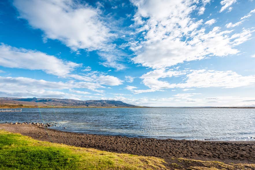 Calm waters of Lake Laugarvatn surrounded by grass under a clear blue sky.