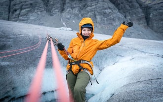 Woman in an orange jacket rappels down the icy surface of Solheimajokull Glacier.