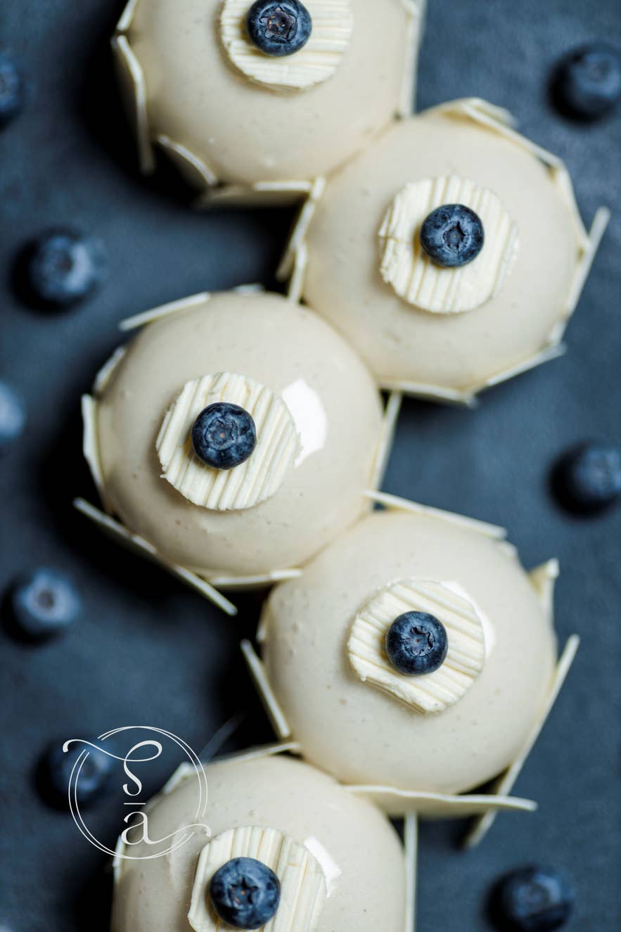 Top view of a white frosted cake with yellow zest and a gold Sweet Aurora seal on a dark wooden surface.