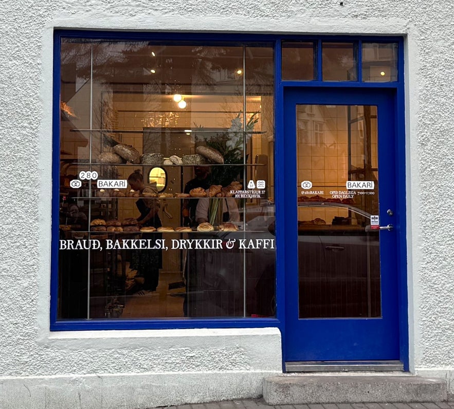 Exterior of 280 Bakery in Reykjavík with blue door, bread display, and warm interior inviting customers inside