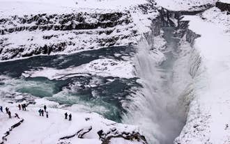 Tourists stand near the edge massive drop of Gullfoss Waterfall in winter.