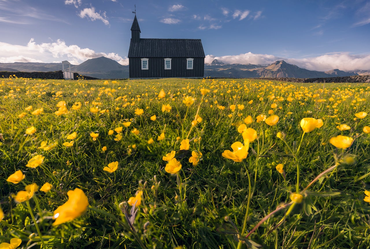 Budakirkja Black Church in early spring with soft sunlight over distant snow-capped mountains.